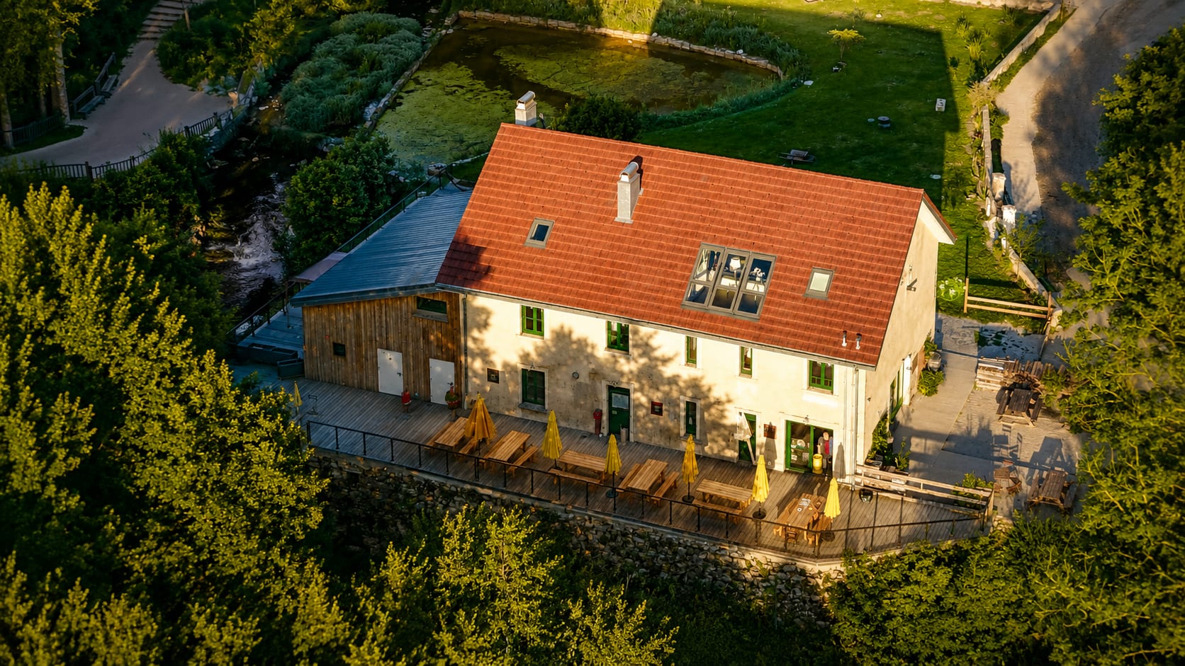 Vue aérienne du Moulin des Fées au coucher du soleil : la terrasse, l’étang et la forêt du Jura